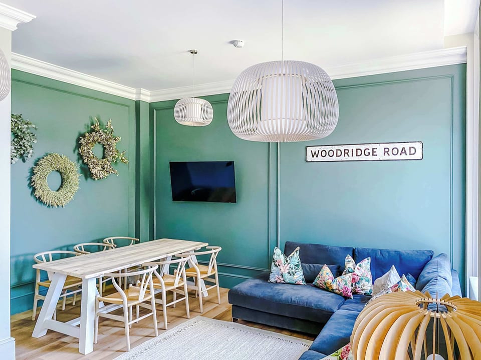 Bright and stylish dining area featuring a spacious wooden table with comfortable seating for family meals or gatherings. Set against elegant green panelled walls with modern lighting, it’s the perfect space to dine, work, or enjoy quality time toget