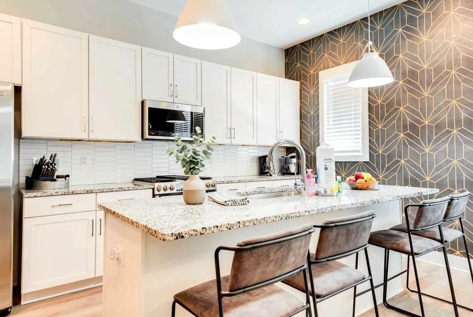 Open kitchen with geometric accent wallpaper and island seating, designed so whoever's making breakfast stays part of the group conversation