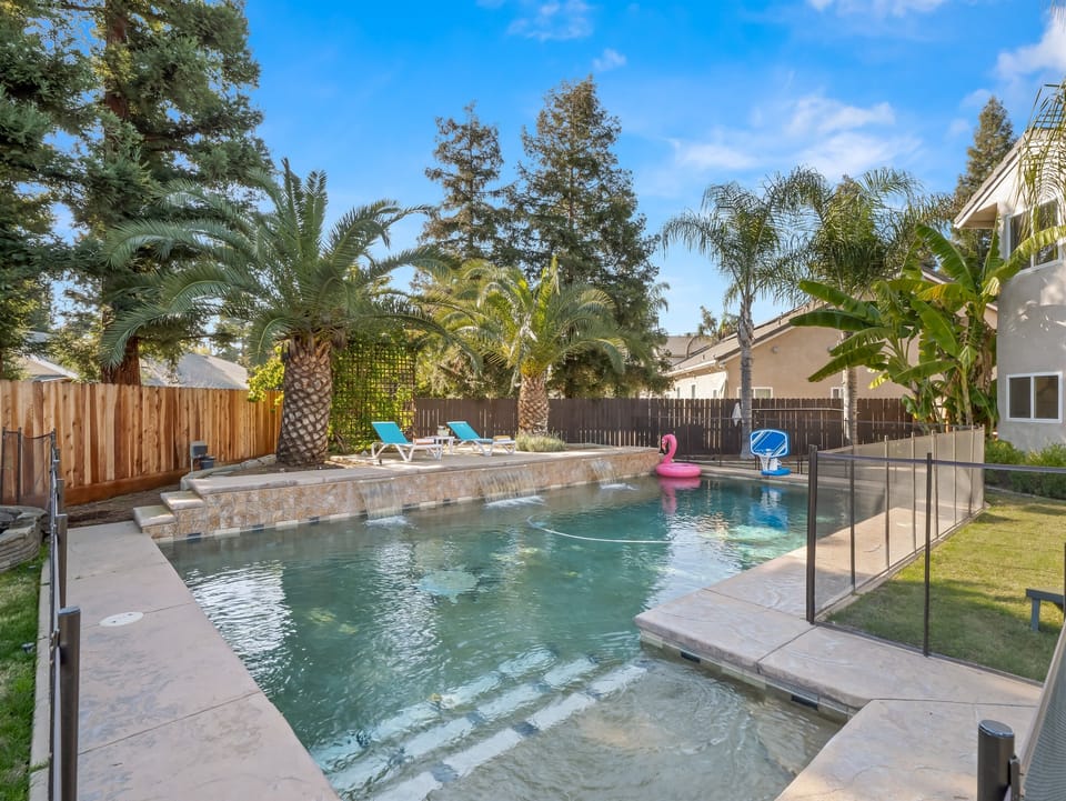 Private backyard oasis featuring a sparkling pool with waterfalls, lounge chairs, and tropical landscaping.