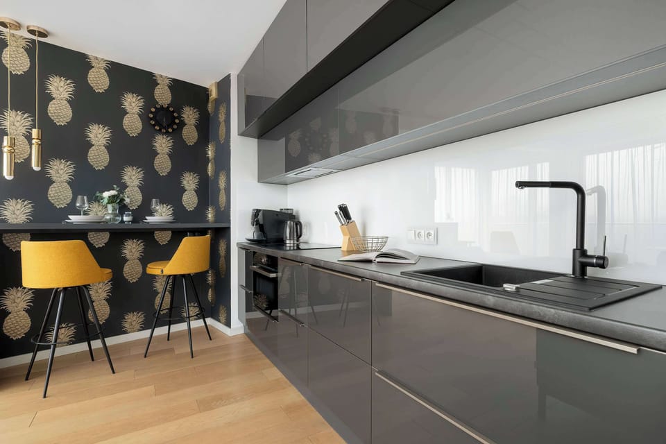A dining area next to a modern kitchen, highlighted by patterned wallpaper and yellow chairs that add a pop of color.