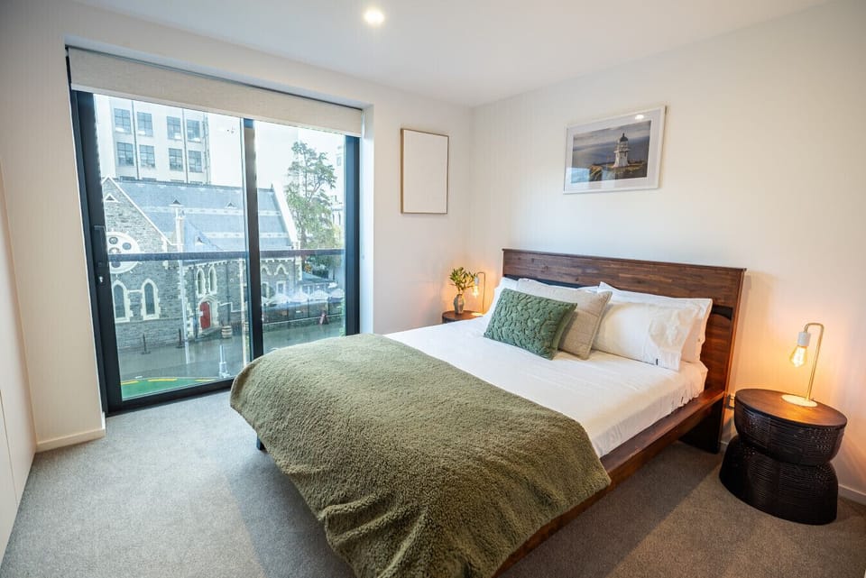 Bright and peaceful queen bedroom with floor-to-ceiling windows overlooking Manchester Street. A queen comfortable bed, warm lighting, and natural tones create a relaxing space in the heart of the city.
