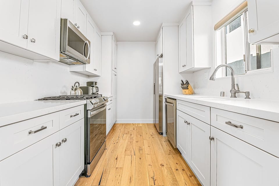 Bright white galley kitchen with sleek stainless steel appliances
                