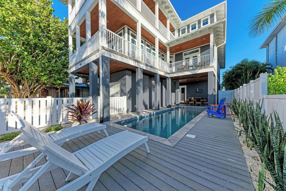 A modern tropical rental home featuring a private pool, spacious deck, and lush landscaping under clear blue skies.