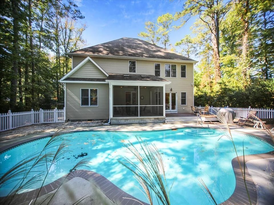 Rear exterior view shows a private backyard pool with surrounding deck space and the spacious two-story home nestled among mature trees.