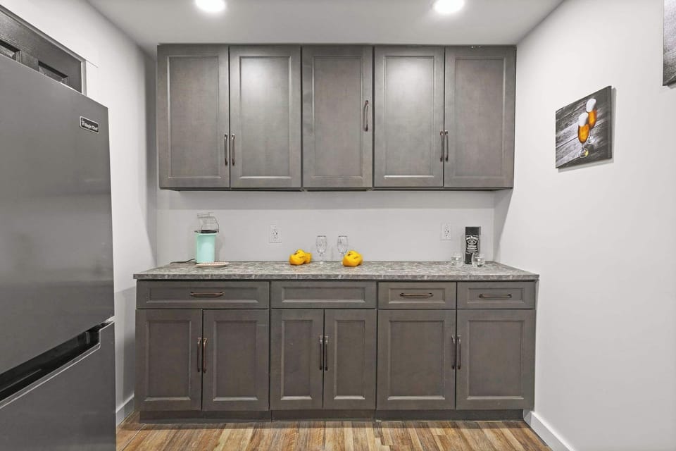 Secondary bar area with dark gray cabinets, stainless fridge, and granite counter
