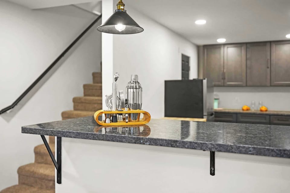 Kitchen bar counter with dark granite top and pendant lighting near staircase