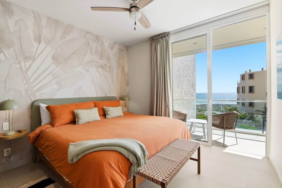 Relax in this comfortable king bedroom with air conditioning, ceiling fan, convenient bedside light switches and outlets for charging devices, plus direct access to your private balcony with ocean views.