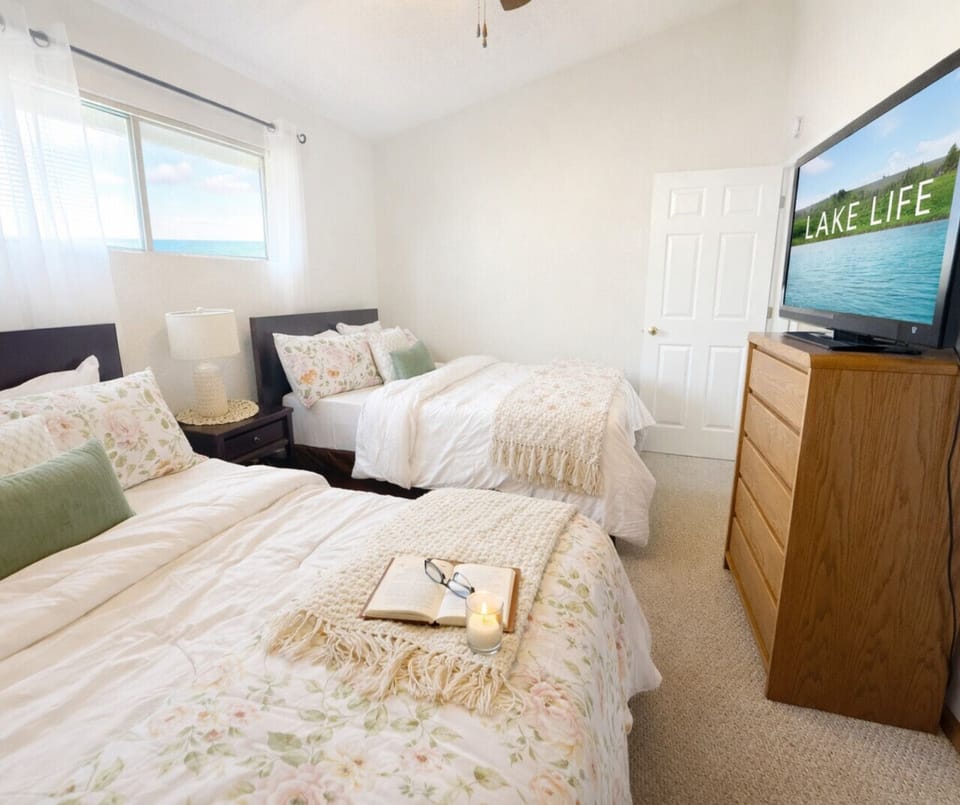 Bright guest bedroom with two comfortable beds, natural light, and TV—perfect for families, groups, and comfortable multi-guest vacation stays.
