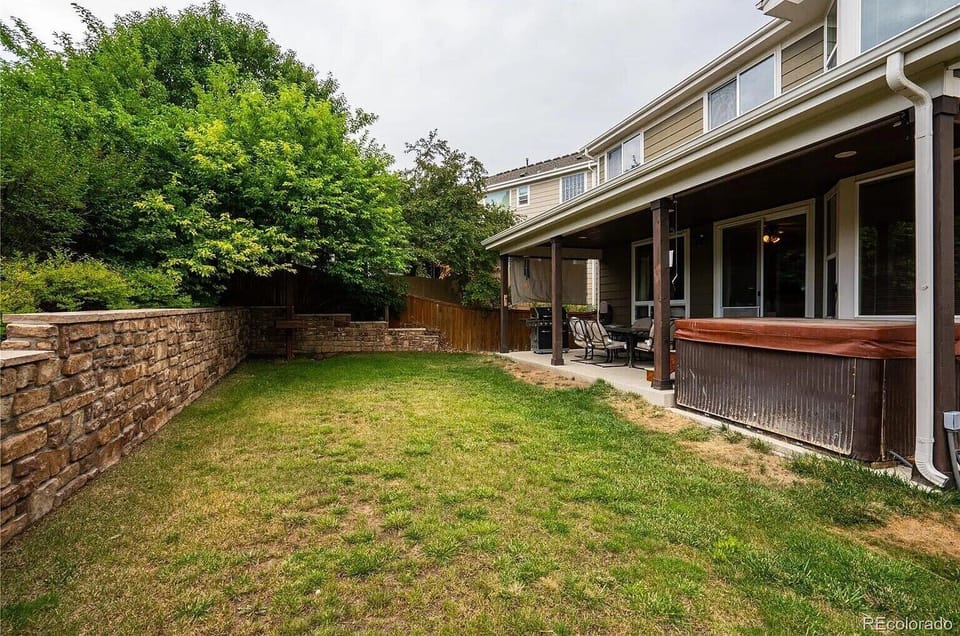 Your private backyard oasis features a spacious lawn perfect for outdoor activities, surrounded by mature trees and enclosed by elegant stonework.