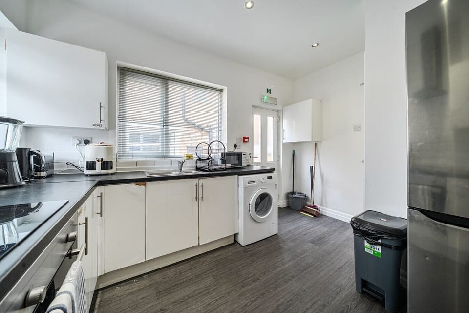 The kitchen worktop area laid out with small appliances including a kettle, microwave and toaster, alongside a washing machine and tall fridge-freezer