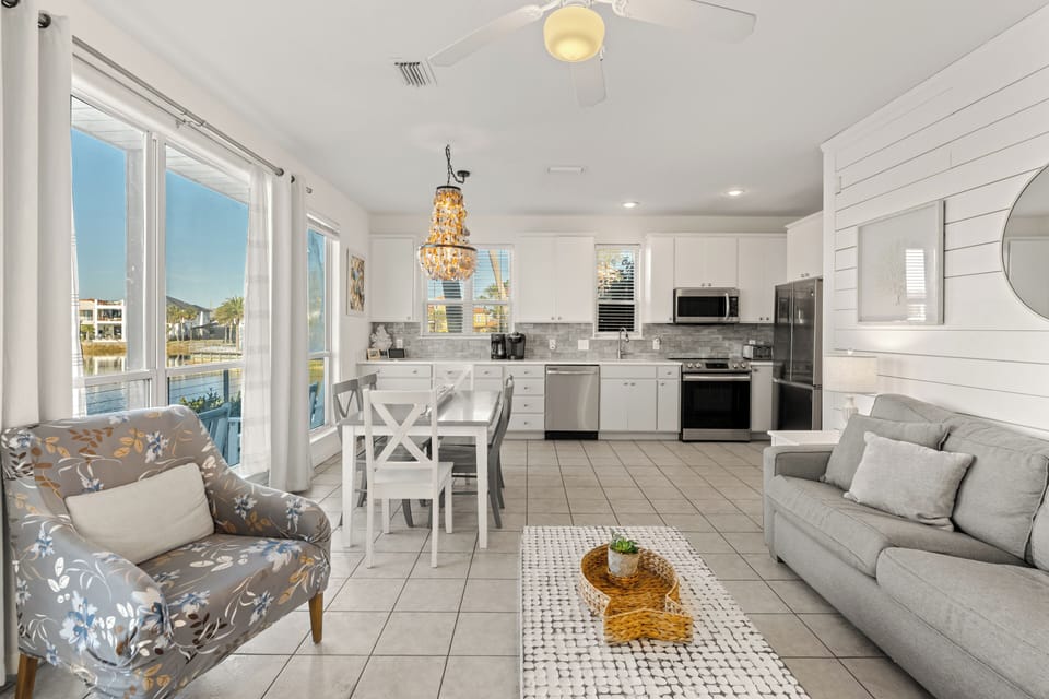 Bright first-floor living room with an open layout, comfortable seating, and large windows that bring in natural light and calming water views.