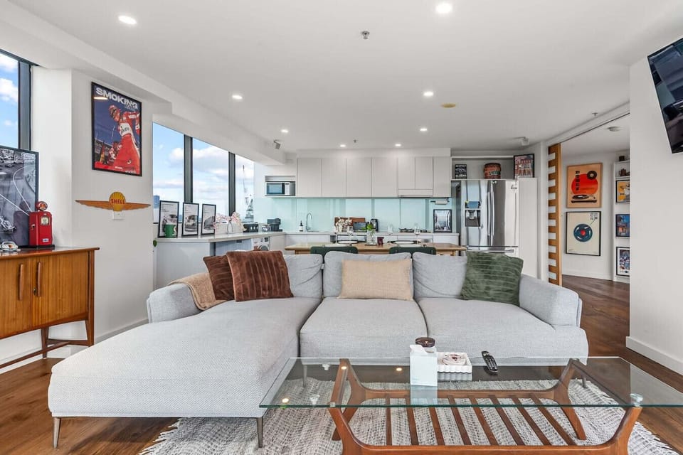 Spacious open-plan living area with a comfortable sectional sofa, dining space, and full kitchen. Large windows bring in natural light and city views, creating an inviting setting to relax, cook, or spend time together indoors.