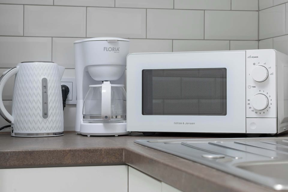 Kitchen countertop with visible electric kettle, pour-over coffee maker, and microwave. All appliances are kept in a bright, consistent color scheme.