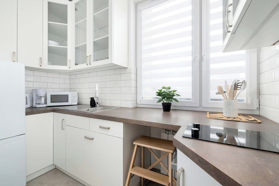 A modern kitchen with white cabinets and a wooden worktop under the window. The kitchen is equipped with a hob, sink, and essential cooking utensils.