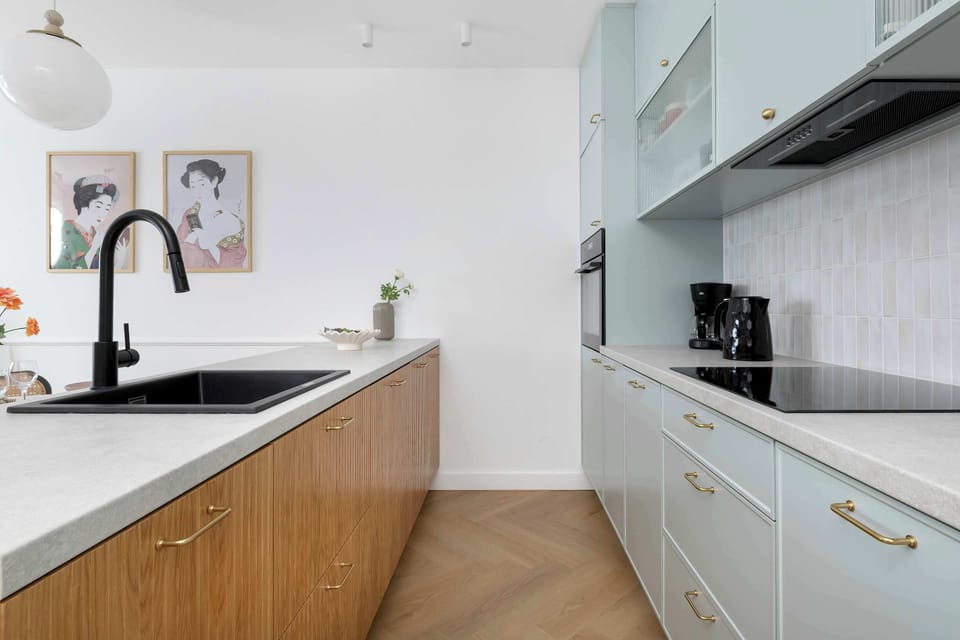 The kitchenette workspace includes a modern black faucet and integrated hob. Wooden lower cabinets contrast beautifully with the cool blue tones of the upper storage units.