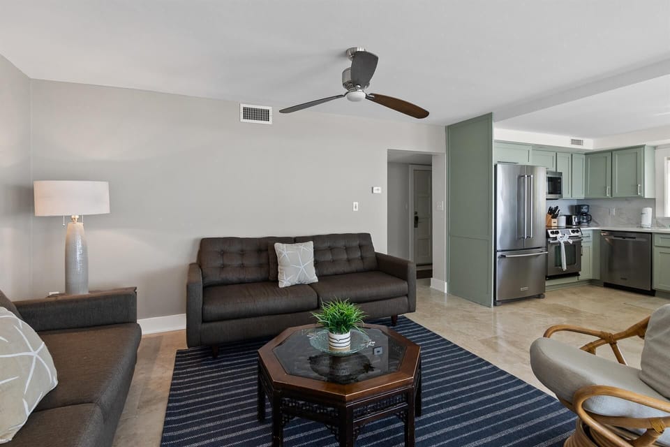 Relax in your spacious living room with modern furniture, ceiling fan, and stylish sage-green kitchen just steps away.