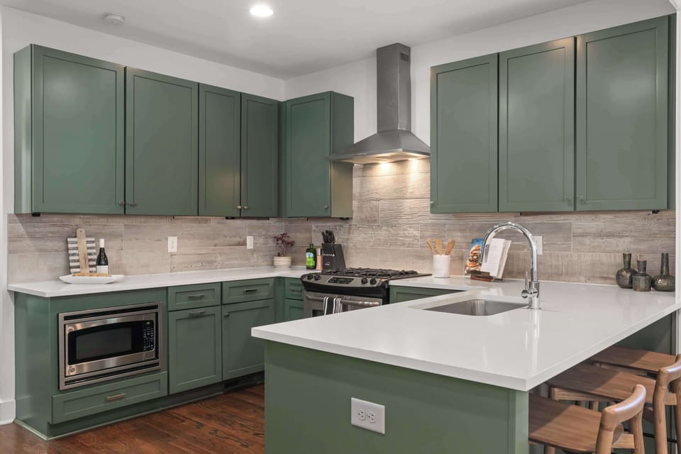 Designer green cabinetry, quartz countertops, and modern finishes create a stylish and functional cooking space.