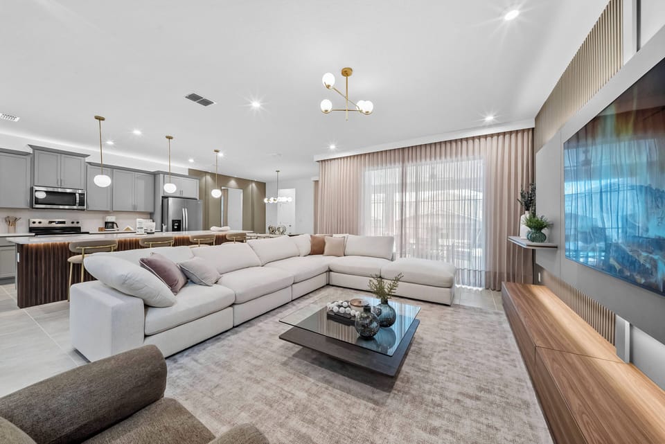 This stylish living room, filled with natural light, features a plush neutral sectional sofa perfect for relaxation. Contemporary decor and sleek wooden accents enhance the atmosphere of comfort and sophistication.
