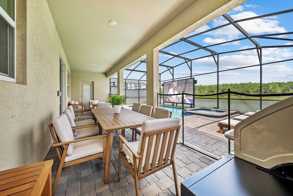 Unwind on the covered patio at the spacious wooden dining table, surrounded by cozy seating. The screened enclosure lets in natural light and offers lovely views of the inviting pool area, creating an ideal retreat.