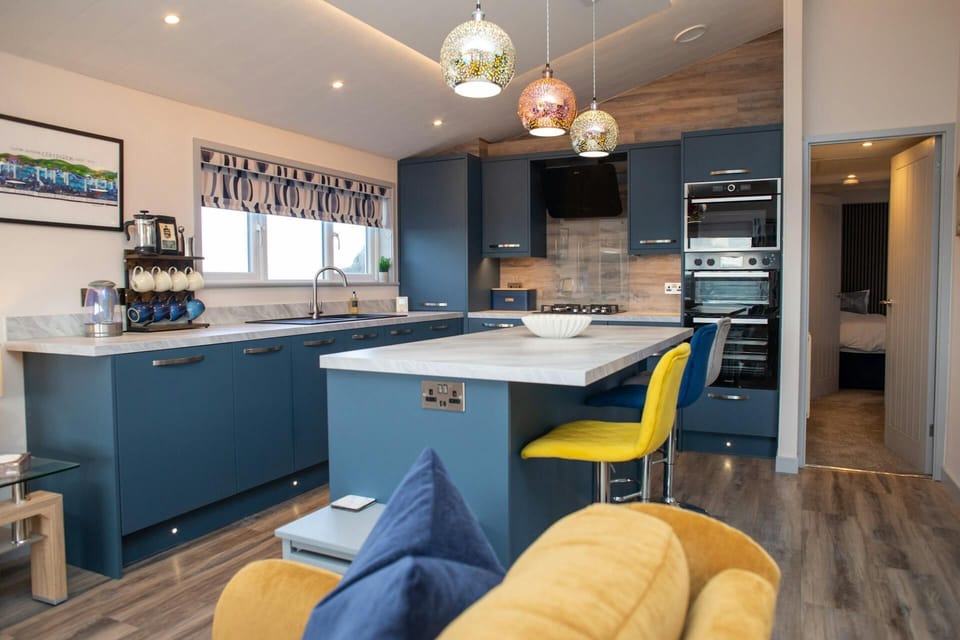View into kitchen from living area, showing island, yellow stool and pendant lights