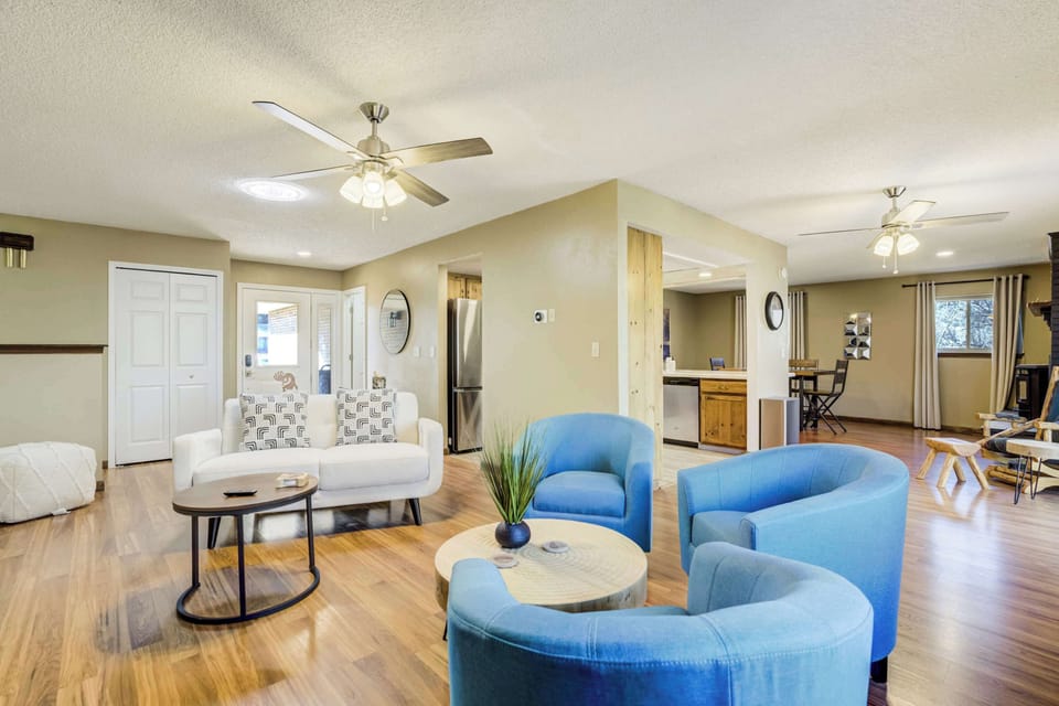 The open-concept living area features a vibrant seating arrangement with a white sofa and three plush blue armchairs. Hardwood flooring runs throughout the space, connecting the lounge to the dining area and kitchen in the background.