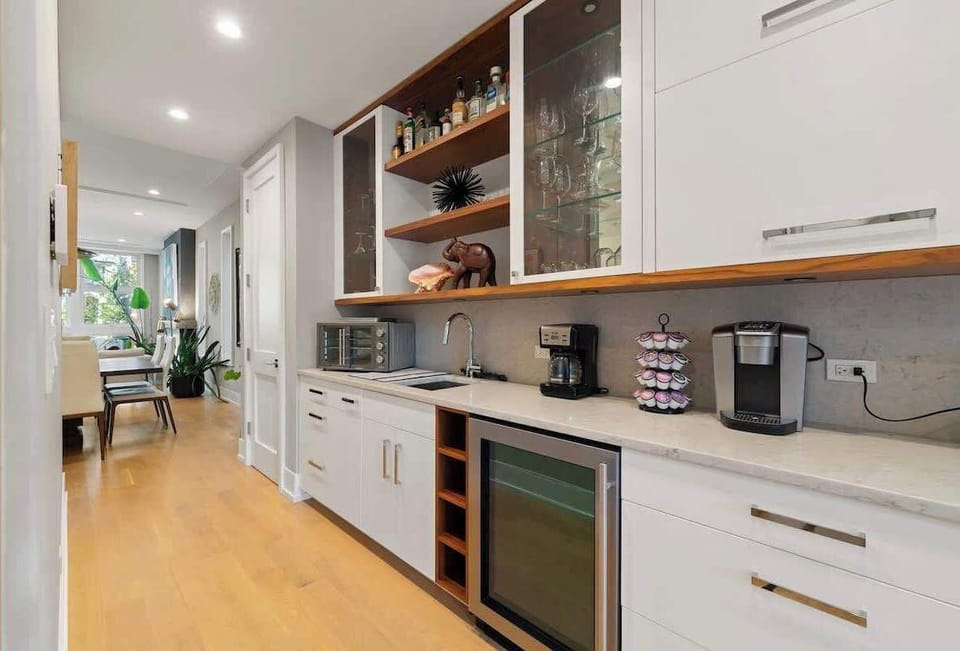 Sleek wet bar w/ wine fridge, coffee setup, & ample storage—great for morning brews or evening pours.