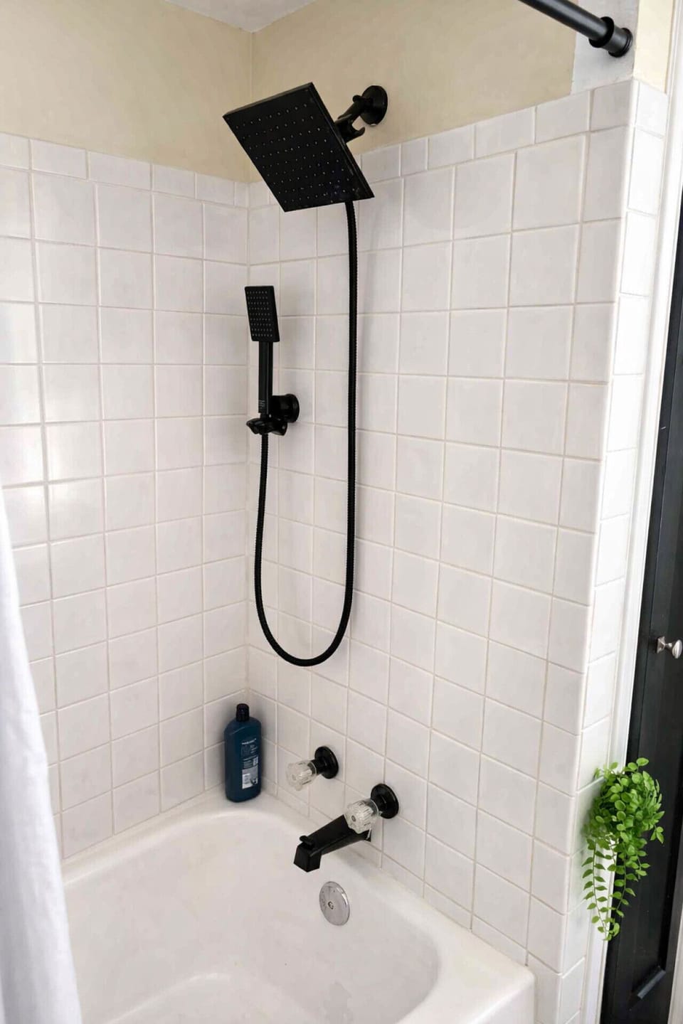 Relax and unwind in this clean, white-tiled tub-shower combo featuring a modern black rainfall showerhead and a convenient handheld sprayer.