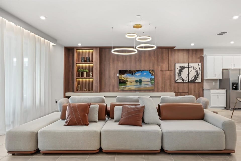 Modern living room with a large sectional sofa and a wood-paneled entertainment wall featuring a flat-screen television.