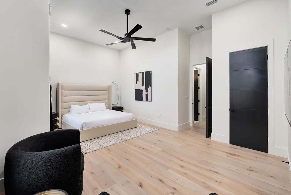 Relax in your sleek modern bedroom with plush bedding, stylish furnishings, and a ceiling fan for perfect comfort.