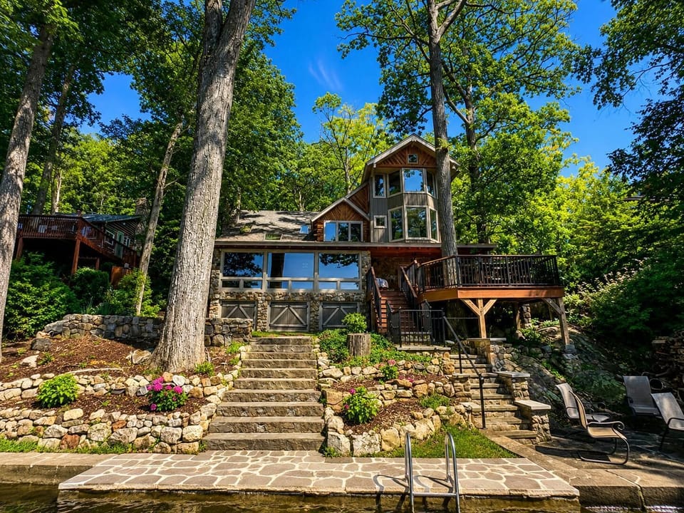 Lakefront exterior with stone stairs, terraced landscaping, wooden deck, and lake access ladder on flagstone dock.