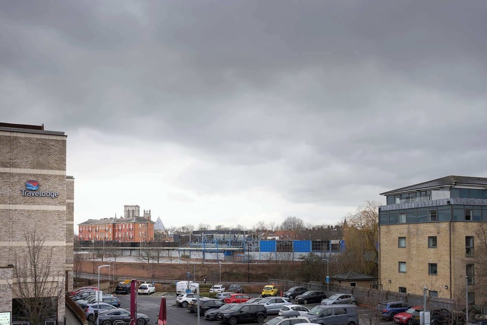 Gaze out from the balcony across the surrounding urban landscape, neighboring buildings, and open parking grounds under overcast skies.