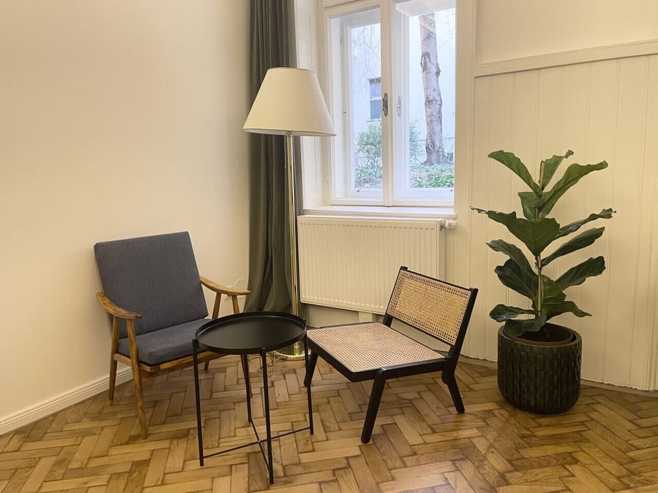 Voll ausgestattete Sitzecke mit Polstersessel, Rattan-Stuhl, Beistelltisch und Stehlampe direkt am Fenster.