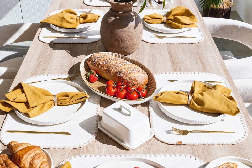 Artisan Breakfast Tablescape

A beautifully curated dining setting featuring textured neutral placemats, elegant gold flatware, and vibrant mustard-yellow linens, centered around fresh artisanal bread and rustic earthenware accents.