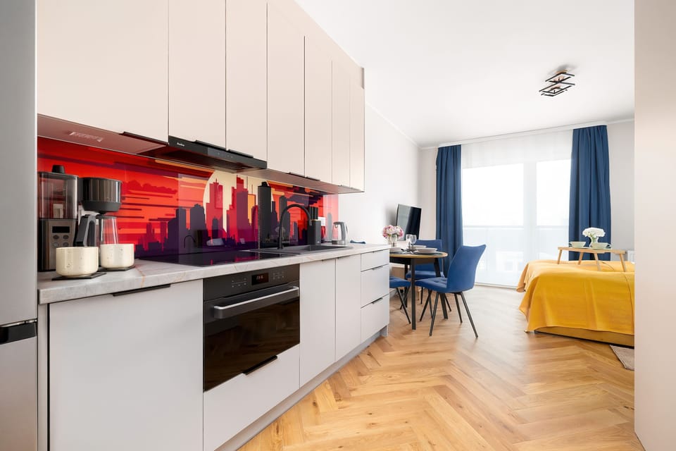 The sleek kitchenette features white cabinetry and a bold red glass backsplash with a city skyline. It is fully equipped with an integrated oven and induction.