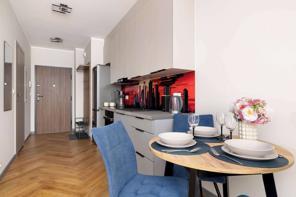 The entryway flows into the dining area, showcasing elegant light wood herringbone flooring. A round dining table is neatly set, welcoming guests for a meal.
