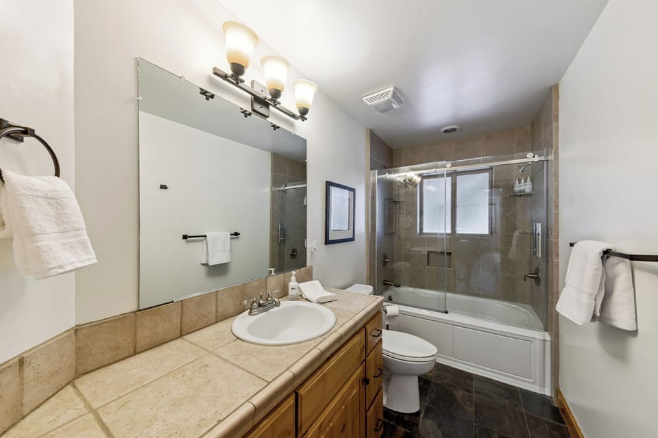 Unwind in your spacious bathroom featuring elegant stone finishes, a deep soaking tub, and glass-enclosed shower with premium fixtures and fluffy towels.