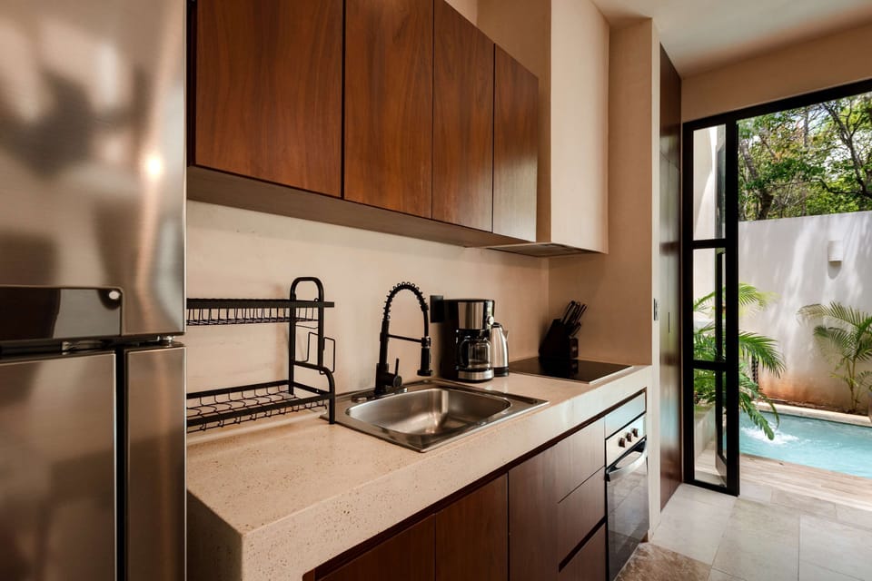 Fully equipped kitchen with built-in appliances and garden pool views through steel-framed window.