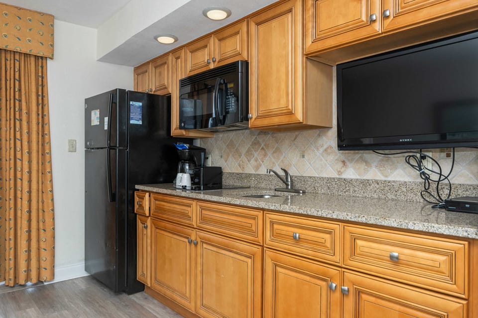 Cozy kitchenette with granite, black appliances, and mounted TV
