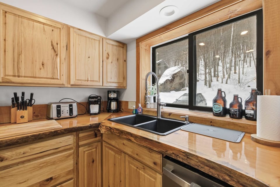 Bright kitchen window overlooks the trees, bringing natural light into the fully stocked space with coffee makers and all essentials.