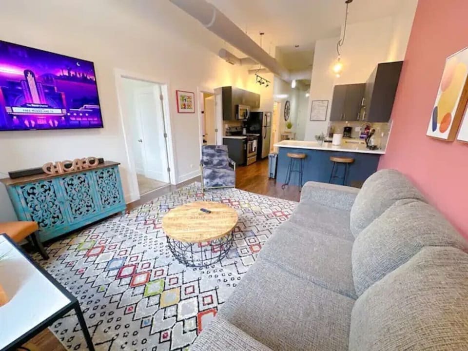 A vibrant living area featuring a comfy sofa, colorful rug, a TV, and an open kitchen with a bold accent wall.