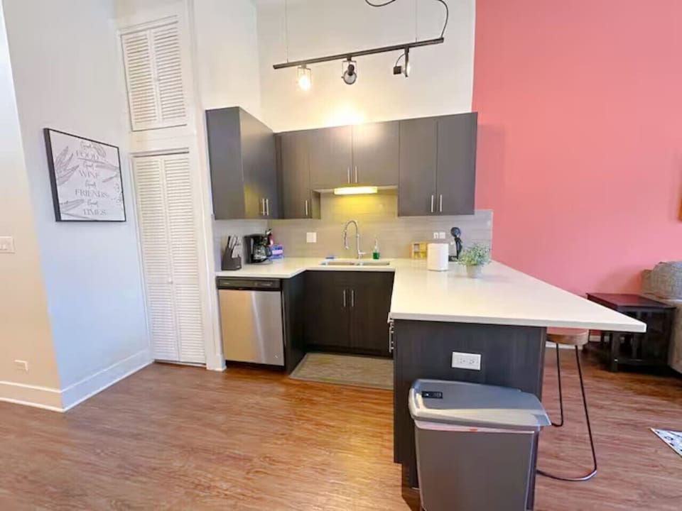 A modern kitchen with dark cabinets, a large island, and a bold pink accent wall.