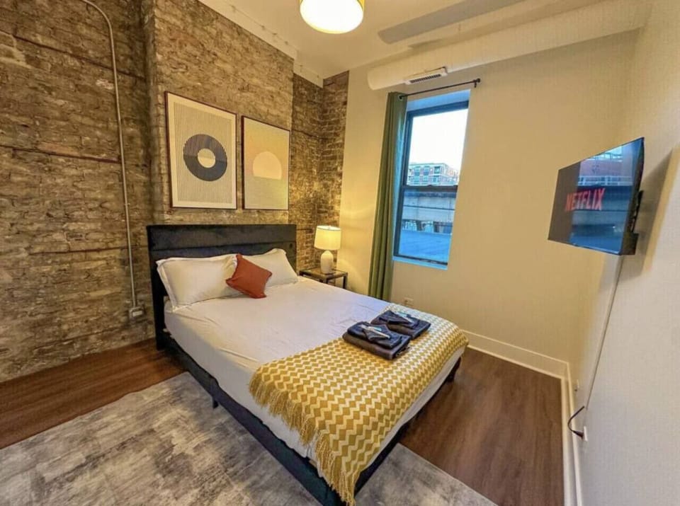 Cozy bedroom with exposed brick, smart TV, and natural light.