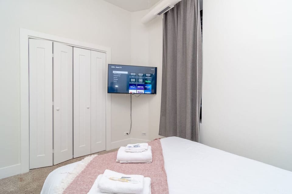 A simple bedroom featuring a wall-mounted TV, a built-in closet, and fresh towels on the bed.