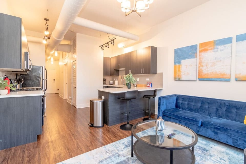 Modern open-concept living area with a stylish kitchen, breakfast bar, and cozy blue sofa seating.