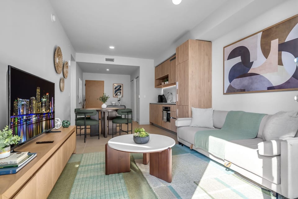 Bright & modern living area with a large TV, plush sofa, and natural light. This open-concept space includes a dining area and a full kitchen, perfect for your comfortable stay!