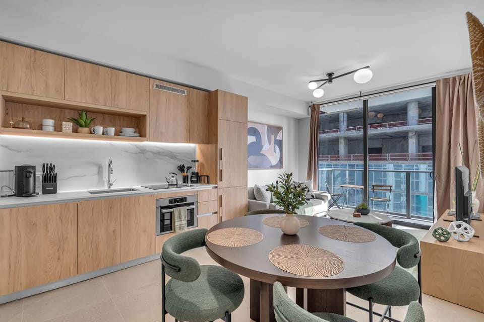 Dine and unwind in this gorgeous open-concept space! Featuring a fully equipped modern kitchen with sleek wood cabinetry, a chic round dining table for four, and a sunlit living area that flows directly onto your private balcony.