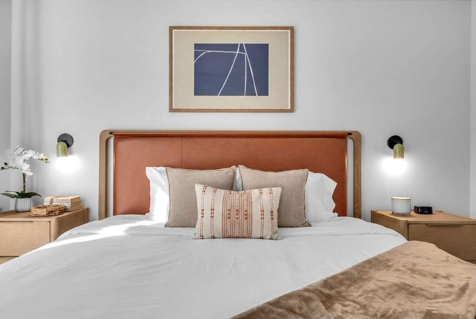 Sink into ultimate comfort in this beautifully styled bed! Complete with a sleek leather headboard, cozy layered pillows, and convenient modern reading sconces on either side. Your perfect relaxing retreat awaits!
