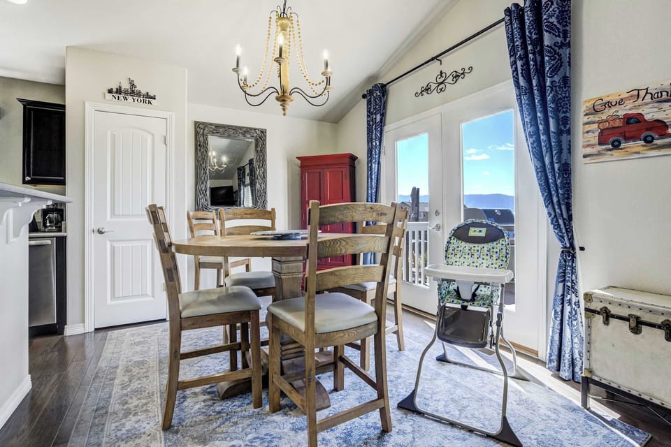 The functional kitchen and dining area features a wooden table with seating for four situated under a tiered chandelier. A raised breakfast bar provides additional counter space and a casual spot for quick meals and a packnplay for the little ones 