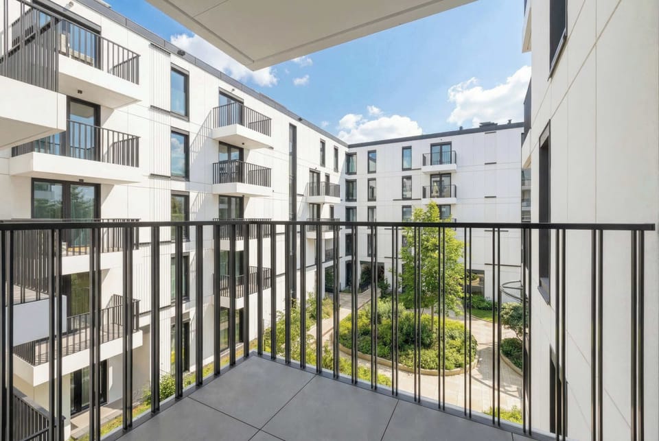 A private balcony with a black metal railing overlooks the beautifully landscaped inner courtyard of the residential complex.