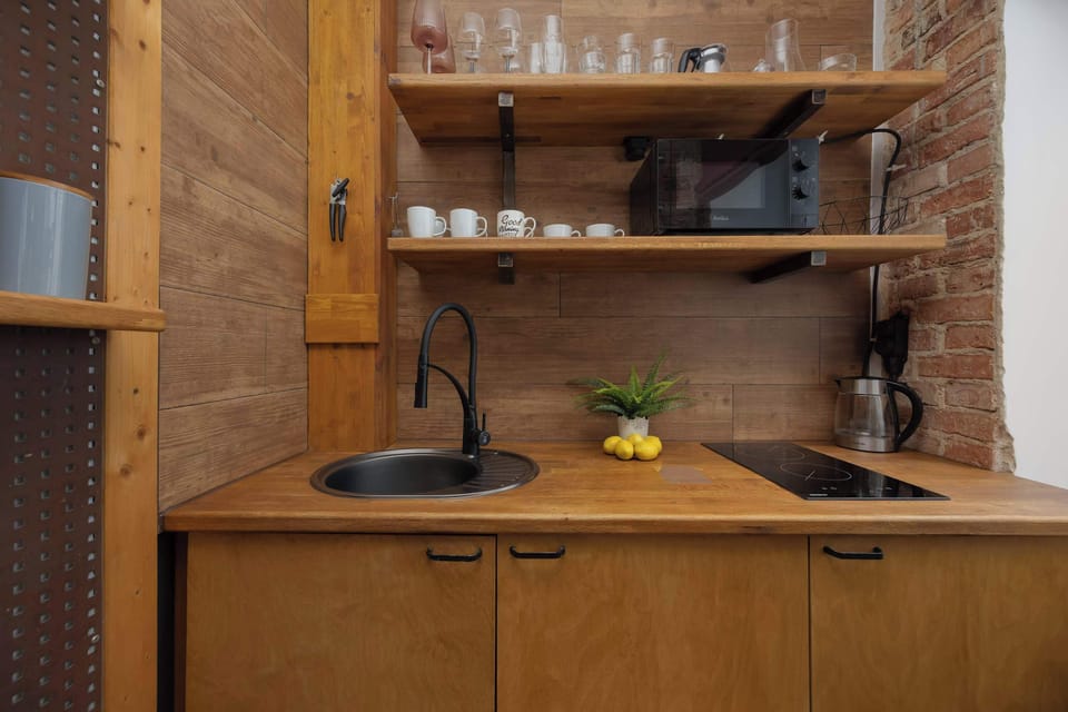 A wooden cabinet with open shelving holding glasses, cups, and a coffee machine on the countertop. The warm lighting highlights the rustic style.